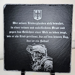 Puede incluir: Placa de pizarra negra con una imagen grabada en blanco de un soldado y una cita en alemán: "Wer seinen Kinderglauben sich bewahrt, in einer reinen und unbefleckten Brust und gegen das Gelächter einer Welt zu leben wagt, wie er als Kind geträumt, bis auf den letzten Tag, das ist ein Soldat!"
