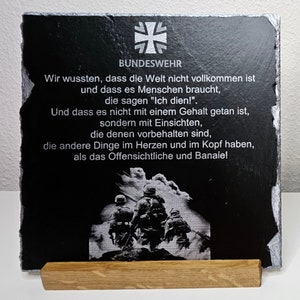 Puede incluir: Placa de pizarra negra con una inscripción blanca y una imagen blanca de soldados marchando. La inscripción dice "Bundeswehr" y "Wir wussten, dass die Welt nicht vollkommen ist und dass es Menschen braucht, die sagen "Ich dien!" Und dass es nicht mit einem Gehalt getan ist, sondern mit Einsichten, die denen vorbehalten sind, die andere Dinge im Herzen y en la cabeza tienen, que lo obvio y lo banal!"