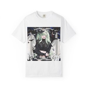May include: White t-shirt with a detailed illustration of a woman with green hair and black clothing. The artwork includes decorative elements and bats, creating a gothic aesthetic. The shirt is made of a soft, comfortable material.