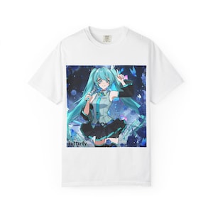 Op de afbeelding: Wit t-shirt met een kleurrijke anime-stijl illustratie van een vrouwelijk personage met lang turquoise haar, die een microfoon vasthoudt. Het personage draagt een zwart-blauwe outfit. Het woord "butterfly" staat onderaan gedrukt.