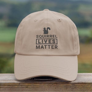 May include: A beige baseball cap with a black silhouette of a squirrel and the text "Squirrel Lives Matter".