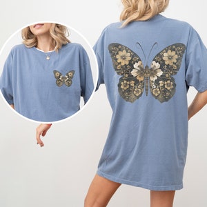 Pu&ograve; includere: Una maglietta oversize di colore azzurro chiaro con un design a farfalla floreale sul retro. La farfalla &egrave; composta da fiori dorati e marroni.