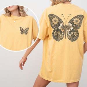 Pu&ograve; includere: Una maglietta gialla oversize con un design a farfalla floreale sul retro. La farfalla &egrave; in tonalit&agrave; di marrone e nero.