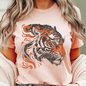 May include: A pink t-shirt featuring a vintage-style graphic of a tiger's head. The tiger is black and orange with a distressed look.
