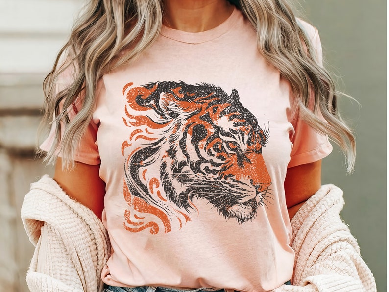 May include: A pink t-shirt featuring a vintage-style graphic of a tiger's head. The tiger is black and orange with a distressed look.