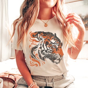 May include: White t-shirt featuring a vintage-style orange and black tiger graphic print.