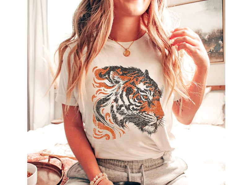 May include: White t-shirt featuring a vintage-style orange and black tiger graphic print.