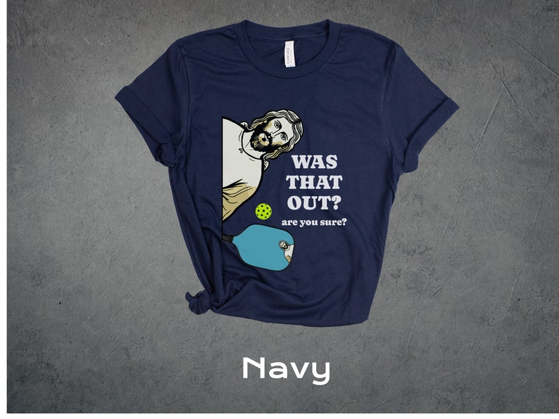 Pu&ograve; includere: Una maglietta blu navy con un'immagine di cartone animato di Ges&ugrave; che gioca a pickleball. Il testo sulla maglietta recita "Was that out? are you sure?"