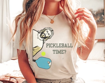 May include: White t-shirt featuring a graphic of Jesus holding a pickleball paddle and a yellow ball. The text "Pickleball Time?" is printed below the graphic.