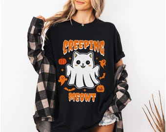 May include: Black t-shirt with a white ghost cat wearing a cute expression. The text "CREEPING MEOWT" is printed on the shirt with orange pumpkins and ghosts.
