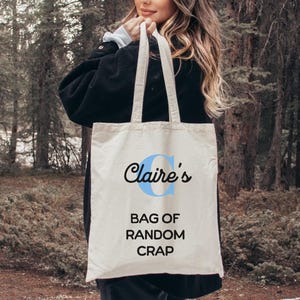 May include: A white canvas tote bag with blue lettering that says "Claire's Bag of Random Crap".