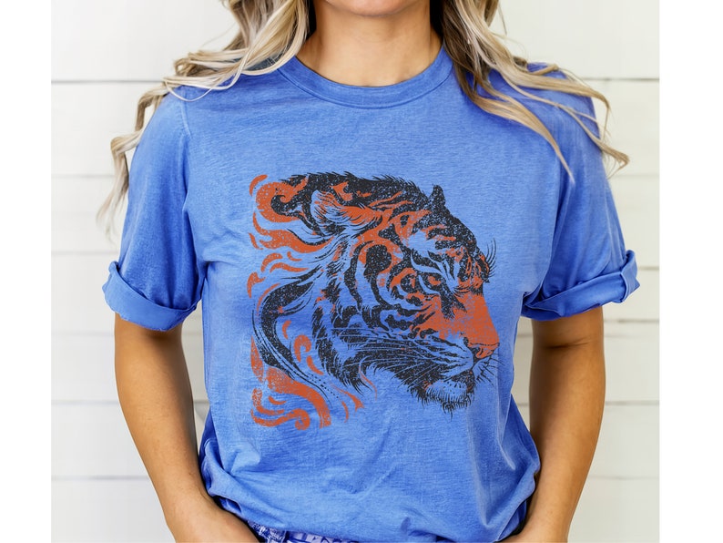 May include: A blue t-shirt featuring a graphic of a tiger's head in black and orange with a distressed effect.