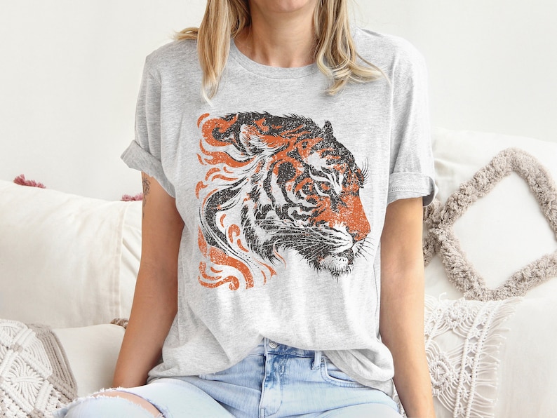 May include: A grey t-shirt featuring a vintage-style orange and black tiger head graphic. The tiger's head is facing to the right and has a distressed look.