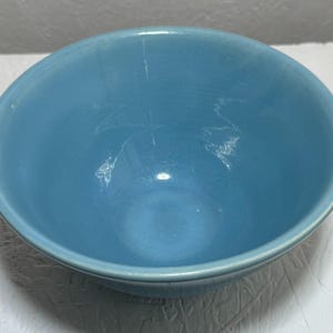 May include: A round, medium-sized ceramic bowl with a smooth, glossy finish in a solid light blue color. The bowl features a simple, open design with a slightly curved rim and a deep, concave interior, showcasing a consistent, uniform blue glaze.