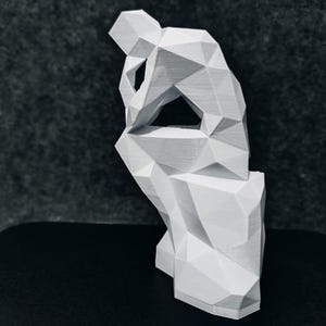 May include: A white geometric sculpture of a person in a seated, contemplative pose. The figure is made of angular planes, giving it a modern, abstract appearance. The sculpture is on a black surface.
