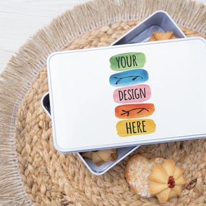 Può includere: Scatola di metallo bianca con un design colorato che dice "YOUR DESIGN HERE". La scatola è aperta e piena di biscotti.