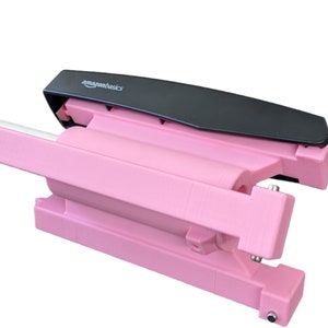 May include: A pink and black plastic device with the text "amazonbasics" on the top. The device is open and appears to be a tool for wrapping or securing items.