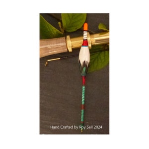 May include: A hand-crafted fishing float with a white body, red and orange accents, and a green and blue striped stem. The float is attached to a fishing rod with a gold reel. The text "Hand Crafted by Roy Sell 2024" is visible at the bottom of the image.