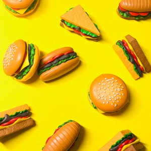 May include: A yellow background with various toy food items, including hamburgers, hot dogs, and sandwiches.