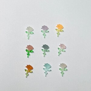 May include: Assortment of nine translucent plastic rose flower charms in various pastel colors, including pink, purple, orange, and green.
