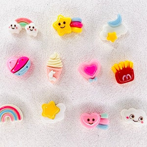 May include: Assortment of colorful resin charms featuring various designs, including a rainbow, a star, a heart, a cloud, a cone, a french fry, and a smiley face.