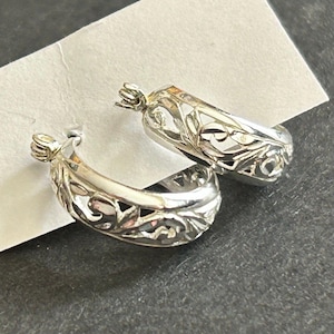 May include: A pair of silver hoop earrings with a delicate floral design. The earrings are made of metal and have a polished finish.