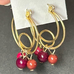 May include: Gold hoop earrings with dangling burgundy and brown beads.