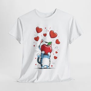 Könnte beinhalten: Weißes T-Shirt mit einer Comic-Katze, die einen roten Apfel hält. Die Katze ist von roten Herzen umgeben.