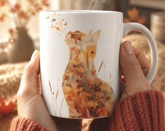 May include: A white ceramic mug featuring a graphic illustration of a cat composed of autumn leaves and wheat stalks. The cat is looking upward toward a small cluster of floating leaves. The mug has a curved handle and a smooth, glossy finish.