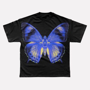 Puede incluir: Camiseta negra con un gran diseño de mariposa. La mariposa tiene alas azules con detalles amarillos, que contrastan con la tela negra. El gráfico está centrado en la camiseta.