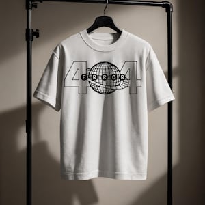 May include: White t-shirt with a black graphic design. The design features the number "404" with a globe in the center and the word "ERROR" inside the globe. The t-shirt is hanging on a black clothing rack.