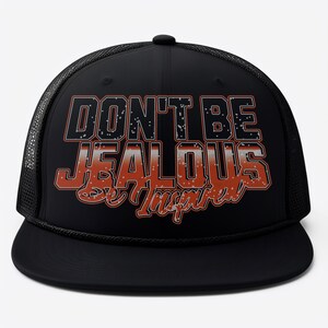 May include: Black trucker hat with a white mesh back. The front of the hat features a red and white graphic that says "Don't Be Jealous Be Inspired".