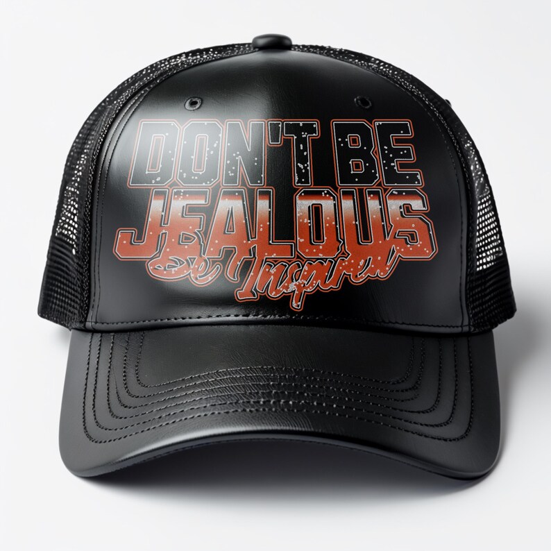May include: Black trucker hat with a black leather bill. The hat has a white mesh back and a red and white graphic that says "Don't Be Jealous Be Inspired".