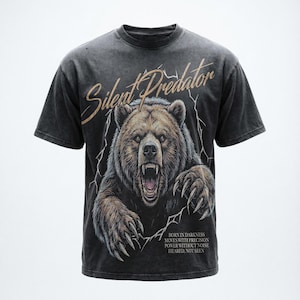 Puede incluir: Camiseta gris oscuro con una ilustración detallada de un oso rugiendo. El texto "Silent Predator" está arqueado sobre el oso, con texto adicional debajo. La camiseta tiene un aspecto vintage y desgastado.