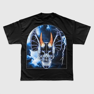 May include: Black t-shirt featuring a graphic of a blue skull with orange horns and bat-like ears against a blue and white stormy sky background.
