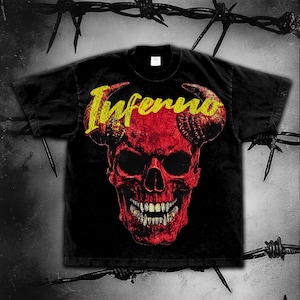 Puede incluir: Camiseta negra con un diseño de calavera roja con cuernos y la palabra "Inferno" en amarillo. La calavera tiene dientes detallados. La imagen está sobre un fondo oscuro con alambre de púas.