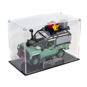 May include: A green LEGO Land Rover Classic Defender 90 model with a black roof rack and various accessories, displayed in a clear acrylic display case with a black base.