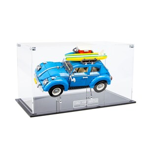 Könnte beinhalten: Ein blaues Lego-Set 1960 VW Käfer mit einem Surfbrett und einer roten und gelben Kühlbox auf dem Dach, ausgestellt in einer durchsichtigen Acryl-Vitrine mit schwarzem Sockel.