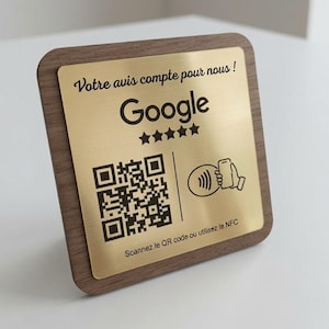 Può includere: Un cartello quadrato con una cornice in legno scuro e una piastra metallica color oro. La piastra presenta il testo "Votre avis compte pour nous !", il logo Google, cinque stelle, un codice QR, un'icona NFC e "Scannez le QR code ou utilisez le NFC".