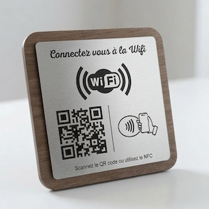 Può includere: Un cartello quadrato con cornice in legno scuro e una piastra frontale in metallo argento spazzolato. Presenta il testo Connectez vous à la Wifi, un simbolo Wi-Fi, un codice QR, un'icona NFC e il testo Scannez le QR code ou utilisez le NFC.