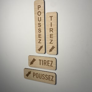 May include: Four wooden signs with arrows and the words "Tirez" and "Poussez" in French. The signs are attached to a white wall.