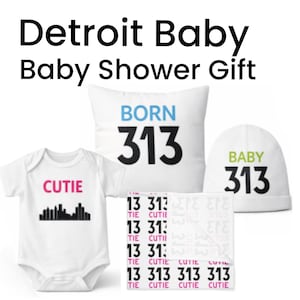 Może przedstawiać: Zestaw prezentowy na baby shower z białym body z napisem "CUTIE" i grafiką linii horyzontu, poduszką z napisem "BORN 313", czapką z napisem "BABY 313" i kocem z tekstem "13 313 CUTIE". Tekst jest w kolorze czarnym, różowym i niebieskim.
