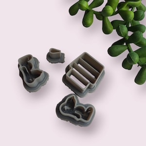 May include: Set of four gray plastic cookie cutters shaped like a house, a heart, and two different flowers.