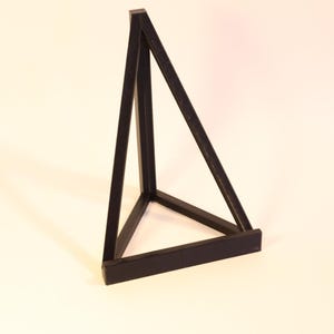 May include: A black, geometric, three-dimensional triangular sculpture. The sculpture is made of solid, dark material and is set against a white background. The design features a base and two angled sides, forming a pyramid shape.