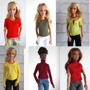 May include: A selection of doll clothing, including tops in red, olive green, and yellow. The tops vary in style, with short and long sleeves, and a sleeveless option. The dolls are styled with different coloured trousers.