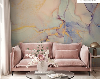 May include: A pink velvet sofa with two pillows sits in front of a wall with a light blue, pink, and gold abstract watercolor design. The sofa is in a living room setting with a coffee table and a lamp.
