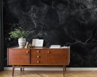 May include: A mid-century modern style wooden dresser with three drawers and two cabinet doors. The dresser is in front of a black marble wall with white veining.