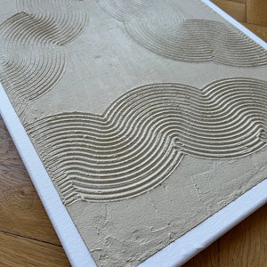 May include: A beige canvas painting with a textured surface. The painting features a pattern of curved lines in a light beige color.