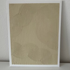 May include: A beige canvas painting with a textured, raised design of overlapping curved lines.