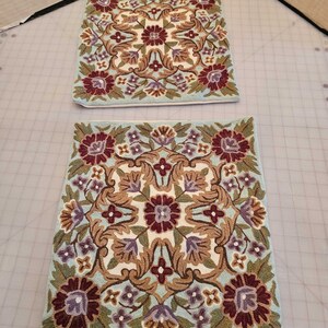 May include: Two square throw pillows with a floral pattern. The pillows are embroidered with a light blue background, brown, green, and purple flowers.